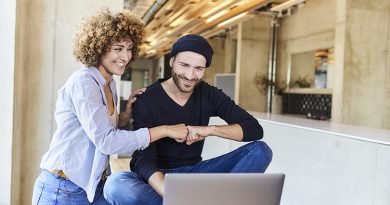 Happy man and woman with laptop fist bumping in modern office