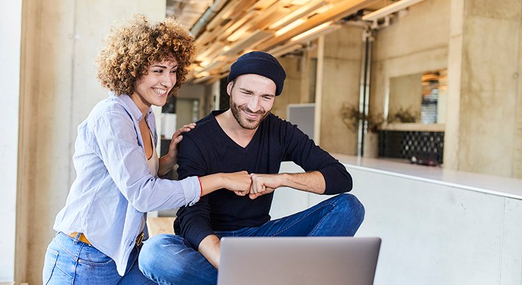 Happy man and woman with laptop fist bumping in modern office